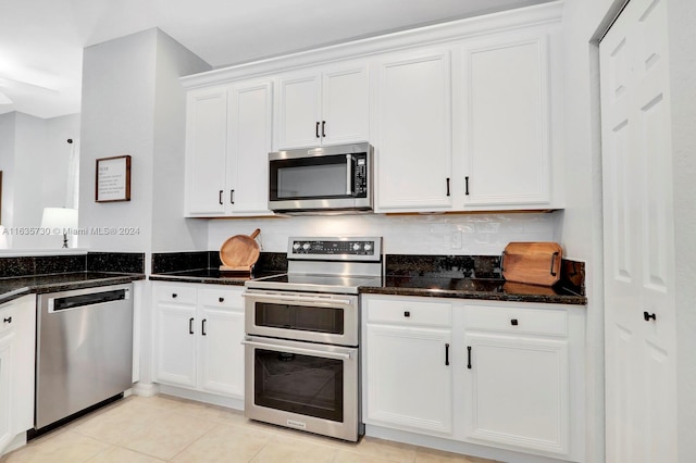 kitchen with dark stone counters, light tile patterned floors, appliances with stainless steel finishes, and white cabinets