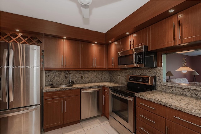 kitchen with appliances with stainless steel finishes, sink, backsplash, light stone counters, and light tile patterned floors