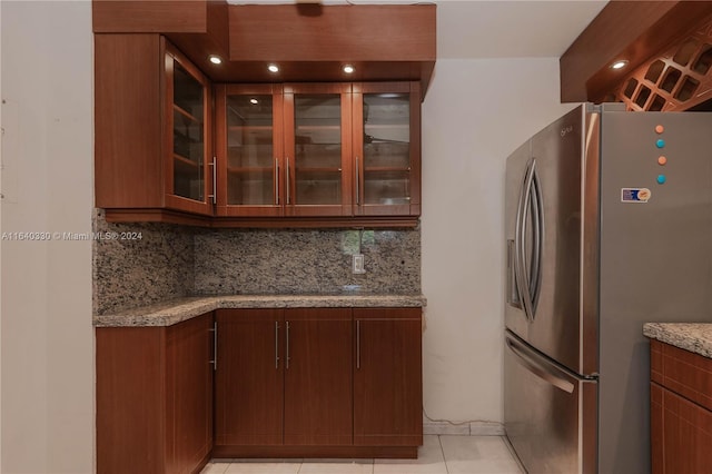 kitchen featuring tasteful backsplash, light stone counters, light tile patterned floors, and stainless steel refrigerator