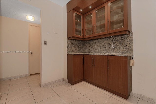 bar with decorative backsplash, light stone countertops, a textured ceiling, and light tile patterned floors