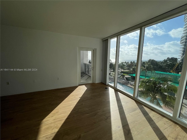 empty room with a wall of windows, wood finished floors, and baseboards