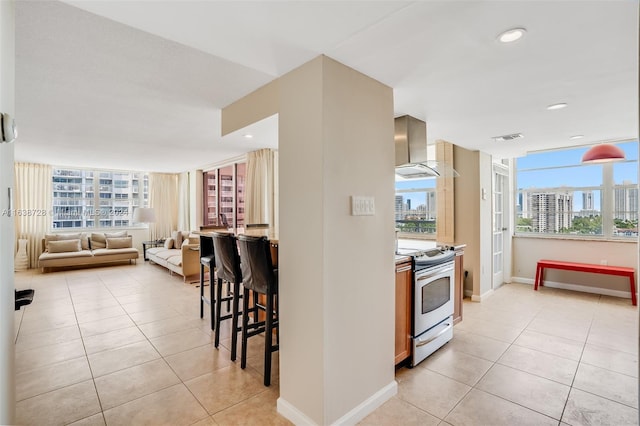 kitchen featuring a kitchen breakfast bar, light tile patterned floors, stainless steel range with electric stovetop, and wall chimney exhaust hood