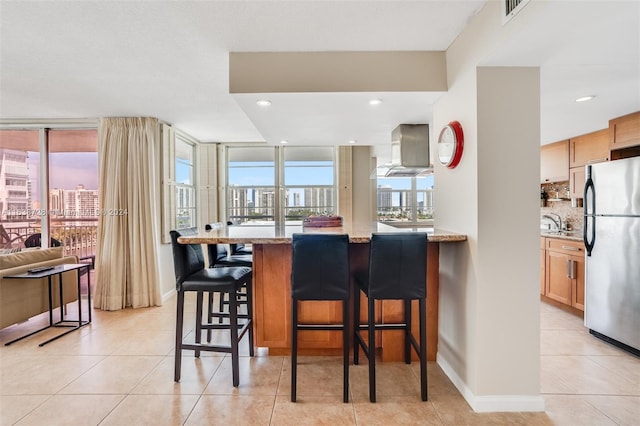 kitchen with a breakfast bar, stainless steel fridge, plenty of natural light, and light tile patterned floors