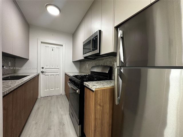 kitchen with appliances with stainless steel finishes, white cabinets, sink, tasteful backsplash, and light hardwood / wood-style floors