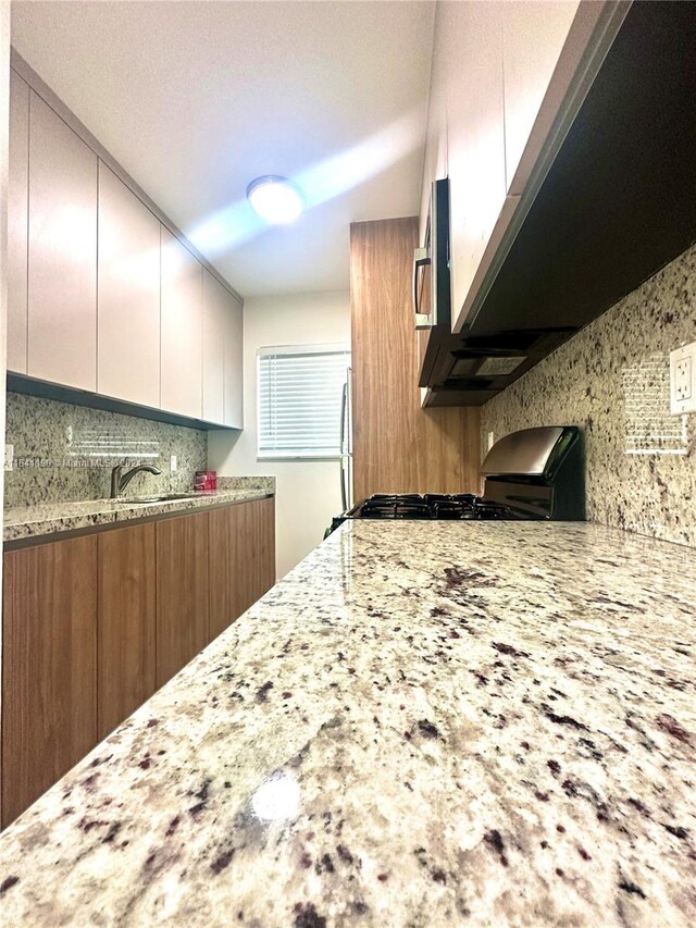 kitchen with decorative backsplash, stove, light stone countertops, and white cabinetry