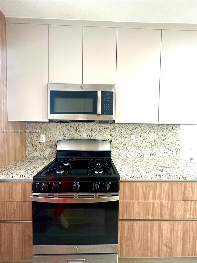 kitchen with decorative backsplash, appliances with stainless steel finishes, white cabinetry, and light stone countertops