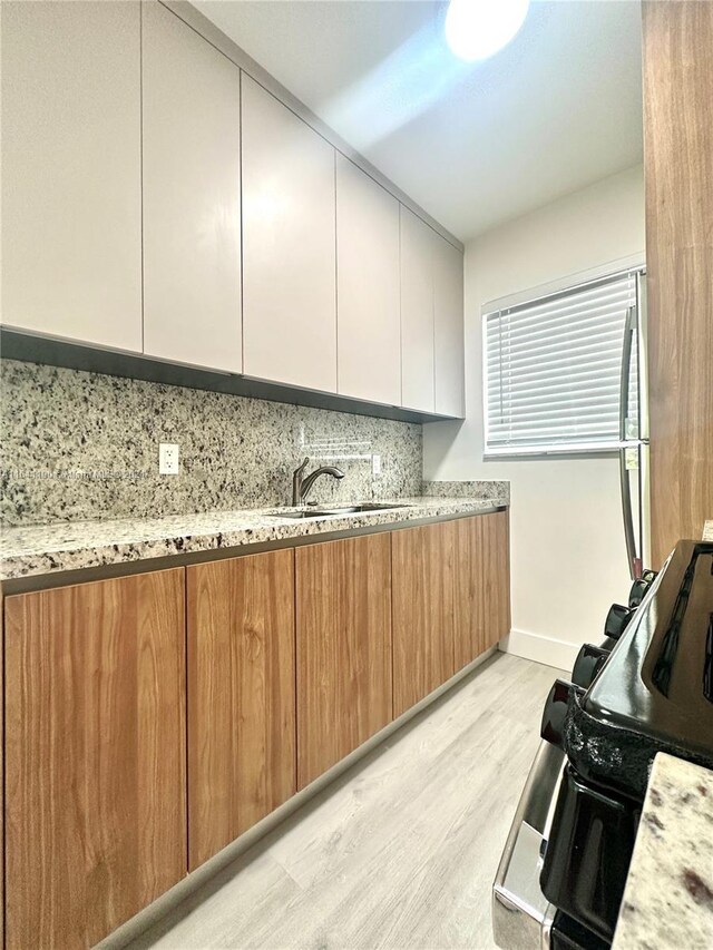 kitchen featuring decorative backsplash, white cabinets, light stone countertops, light wood-type flooring, and sink