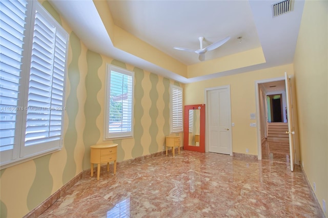 empty room with ceiling fan, tile patterned floors, and a tray ceiling