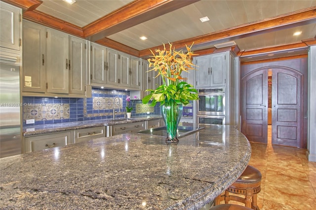 kitchen with beam ceiling, a kitchen breakfast bar, stainless steel appliances, and dark stone countertops