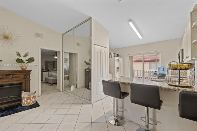 kitchen with white fridge with ice dispenser, light stone counters, a breakfast bar area, vaulted ceiling, and ceiling fan