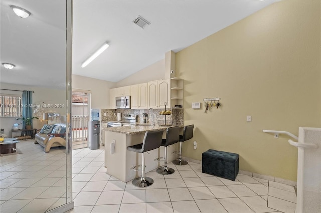 kitchen with a breakfast bar, light stone counters, lofted ceiling, kitchen peninsula, and appliances with stainless steel finishes