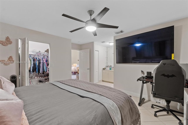 bedroom with a closet, ensuite bathroom, light tile patterned floors, a spacious closet, and ceiling fan