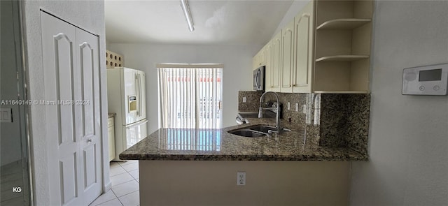 kitchen with appliances with stainless steel finishes, dark stone countertops, tasteful backsplash, kitchen peninsula, and sink