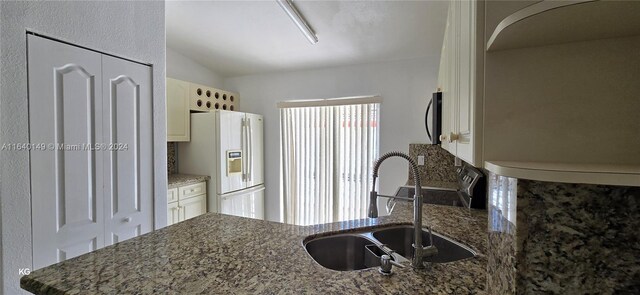 kitchen featuring dark stone counters, white fridge with ice dispenser, plenty of natural light, and sink