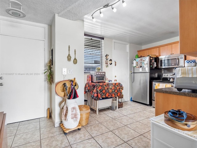 kitchen with appliances with stainless steel finishes, light tile patterned flooring, a textured ceiling, and track lighting