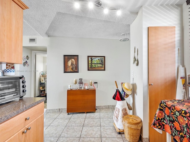 kitchen with a textured ceiling, light tile patterned floors, track lighting, and light brown cabinetry