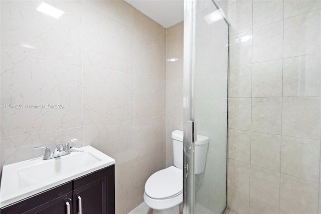 bathroom featuring vanity, a tile shower, toilet, and tile walls