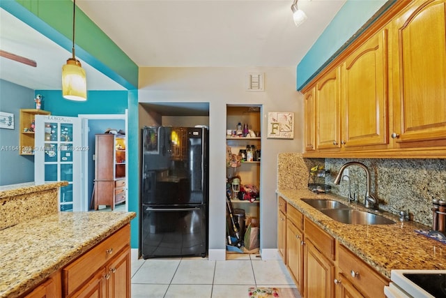 kitchen with light tile patterned floors, light stone counters, a sink, freestanding refrigerator, and decorative backsplash