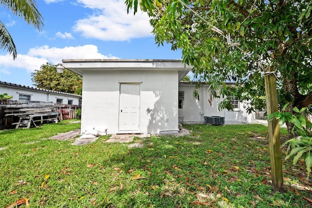 rear view of house featuring a storage shed, central AC, an outdoor structure, a lawn, and stucco siding