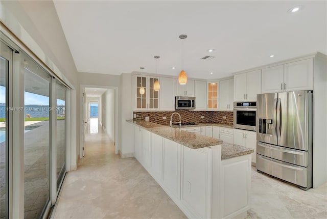 kitchen with kitchen peninsula, light stone counters, stainless steel appliances, decorative light fixtures, and white cabinetry