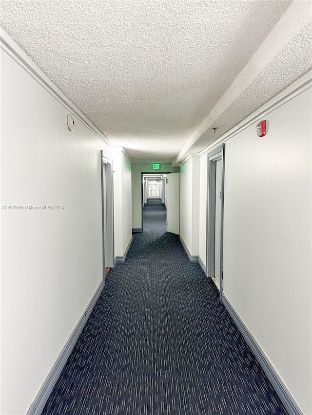 hall featuring a textured ceiling and dark carpet