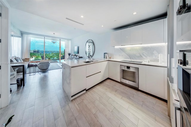 kitchen featuring black electric cooktop, white cabinets, backsplash, oven, and kitchen peninsula