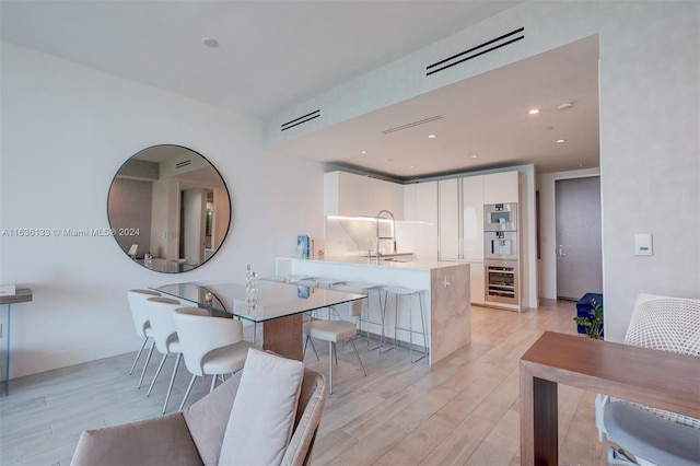 kitchen with stainless steel oven, a kitchen breakfast bar, white cabinetry, light hardwood / wood-style flooring, and kitchen peninsula