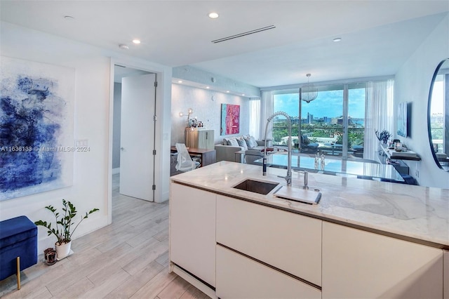 kitchen with light stone counters, light hardwood / wood-style flooring, sink, and white cabinets