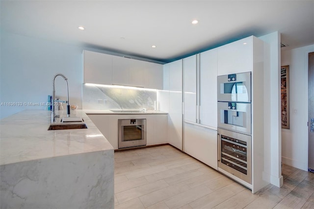 kitchen featuring decorative backsplash, white cabinets, wine cooler, and light stone countertops