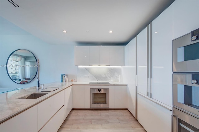 kitchen featuring white cabinets, light stone countertops, stainless steel double oven, black electric stovetop, and tasteful backsplash