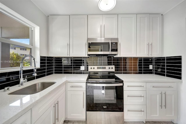 kitchen featuring sink, decorative backsplash, light stone countertops, white cabinetry, and stainless steel appliances