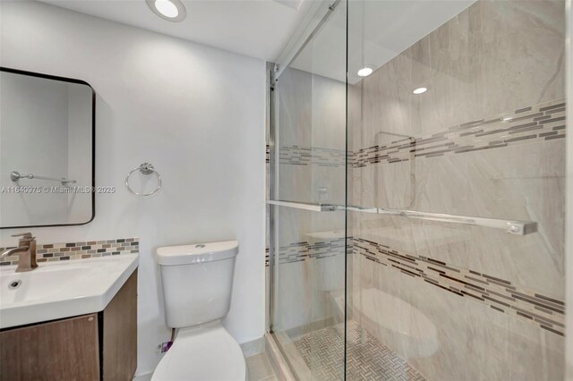 bathroom with vanity, toilet, a shower with door, and backsplash