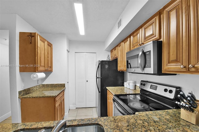 kitchen featuring dark stone countertops, a textured ceiling, light tile patterned floors, sink, and appliances with stainless steel finishes