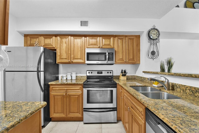 kitchen with a textured ceiling, light tile patterned floors, stainless steel appliances, sink, and dark stone countertops