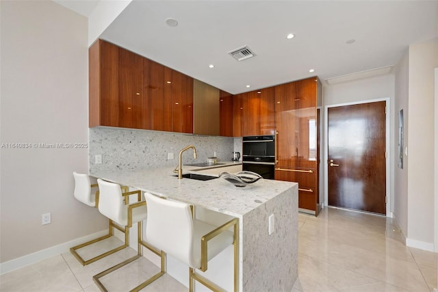 kitchen with dobule oven black, modern cabinets, a peninsula, a sink, and backsplash