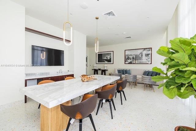 interior space with light speckled floor, a breakfast bar, visible vents, and pendant lighting