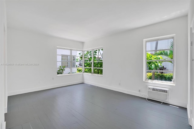 empty room featuring dark wood-type flooring, a wall unit AC, and a healthy amount of sunlight