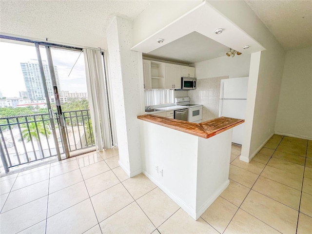 kitchen with stove, decorative backsplash, white cabinetry, fridge, and kitchen peninsula