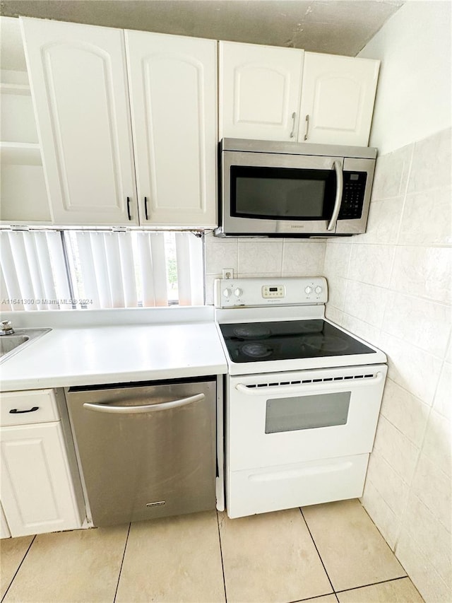 kitchen with light tile patterned floors, tile walls, stainless steel appliances, and white cabinetry