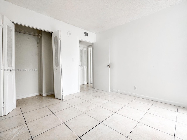 unfurnished bedroom featuring light tile patterned floors, a textured ceiling, and a closet