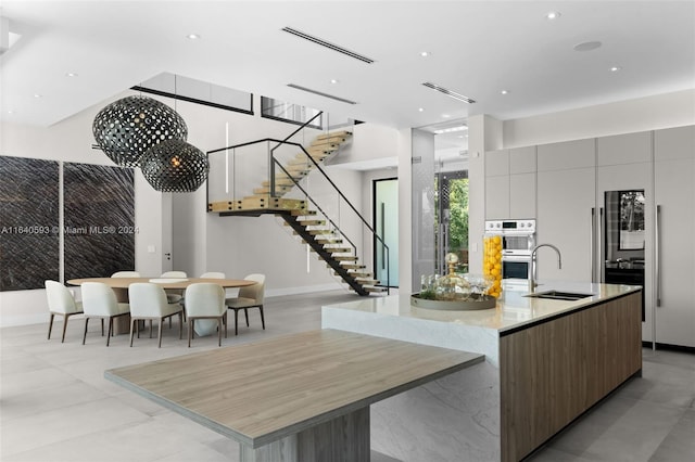 kitchen featuring a spacious island, sink, stainless steel double oven, and light tile patterned floors