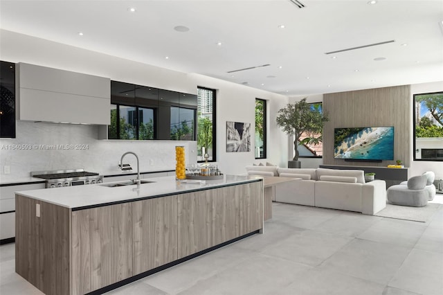 kitchen featuring sink, a center island with sink, backsplash, and range