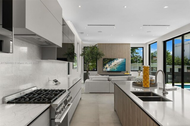 kitchen featuring light stone countertops, sink, tasteful backsplash, wall chimney exhaust hood, and stainless steel range