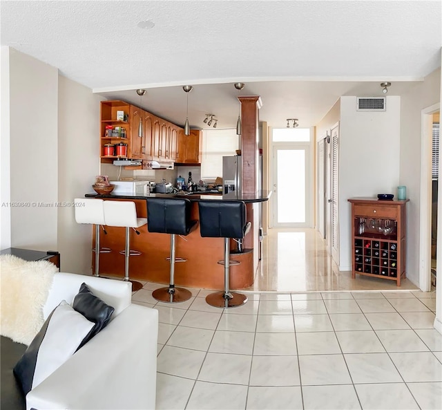 kitchen with decorative light fixtures, light tile patterned floors, kitchen peninsula, stainless steel fridge, and a breakfast bar area