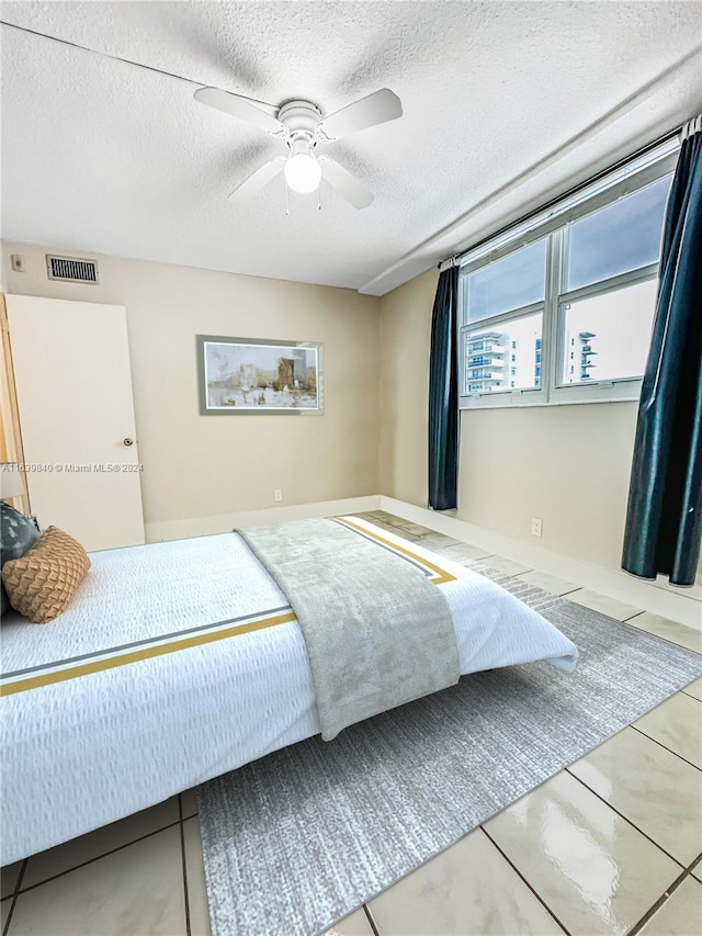 tiled bedroom with ceiling fan and a textured ceiling