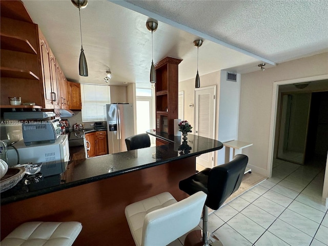 kitchen with stainless steel refrigerator with ice dispenser, hanging light fixtures, light tile patterned floors, kitchen peninsula, and a textured ceiling