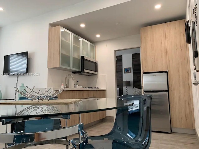 kitchen with light brown cabinetry, appliances with stainless steel finishes, light wood-type flooring, sink, and kitchen peninsula