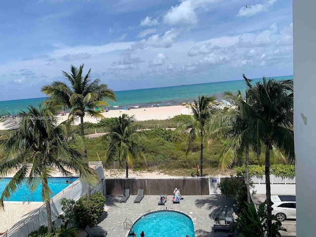 view of swimming pool featuring a water view, a patio area, and a view of the beach