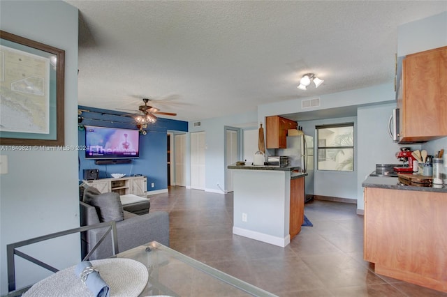 kitchen with appliances with stainless steel finishes, a textured ceiling, ceiling fan, and dark tile patterned floors