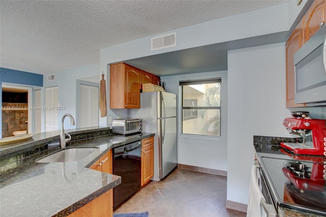 kitchen featuring dark stone countertops, stainless steel appliances, a textured ceiling, light tile patterned floors, and sink